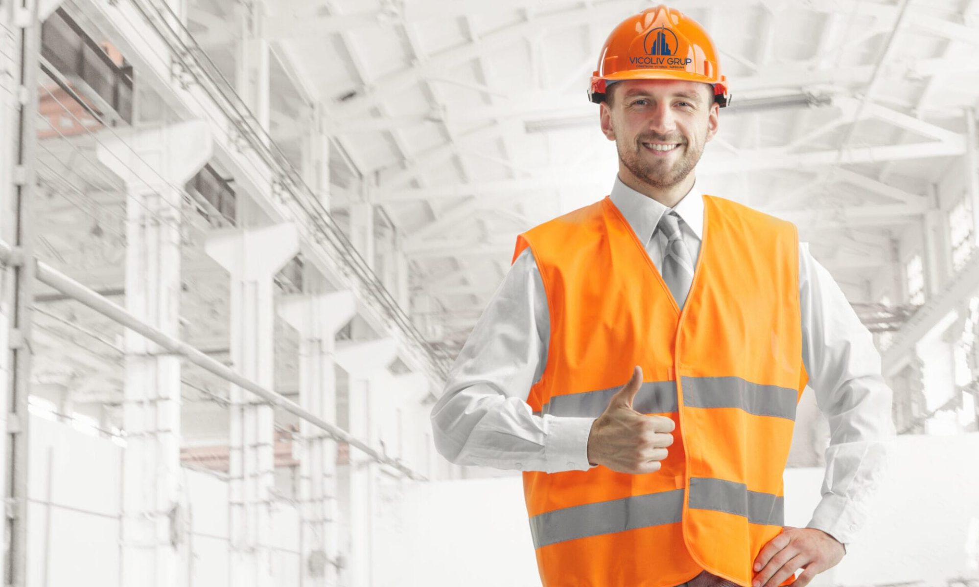The builder in a construction vest and orange helmet smiling with sign ok against industrial background. Safety specialist, engineer, industry, architecture, manager, occupation, businessman, job concept